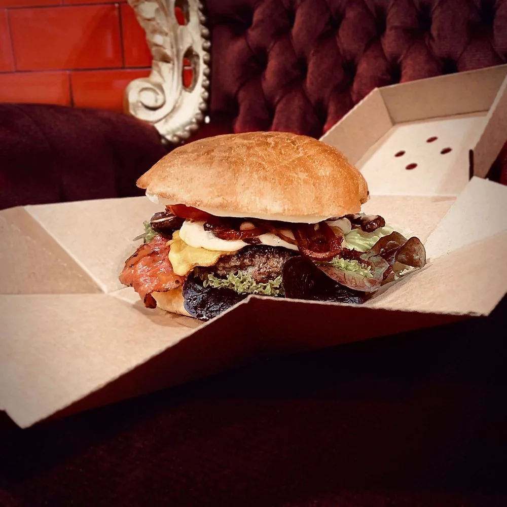 Burger in einer Pappbox auf einer burgunderroten Samtbank
