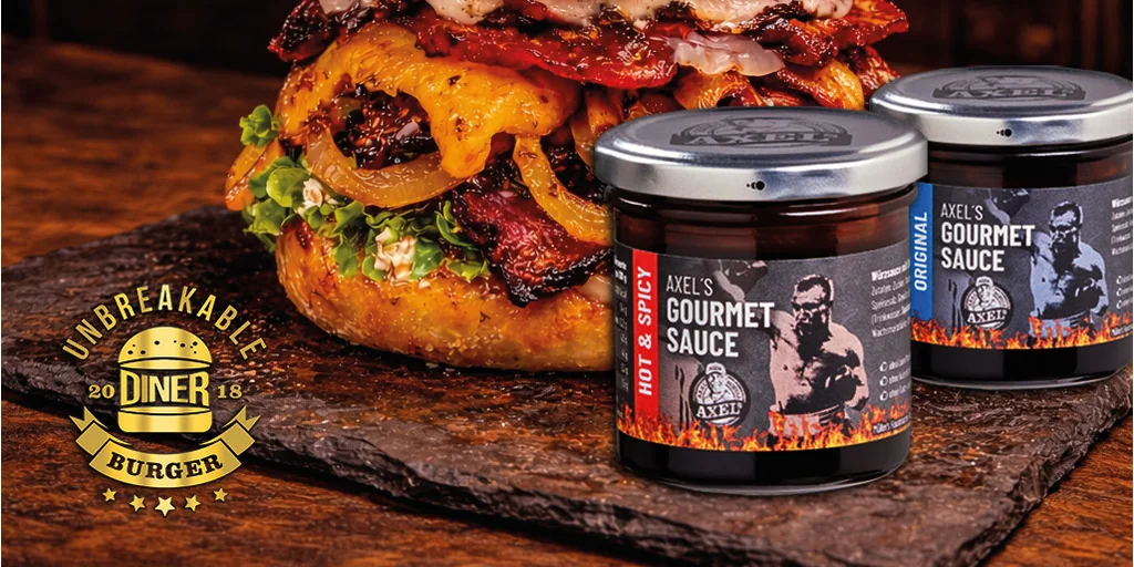 Heavyweight Champ Burger auf einer Schieferplatte, daneben zwei Gläser Axel's Gourmet Sauce