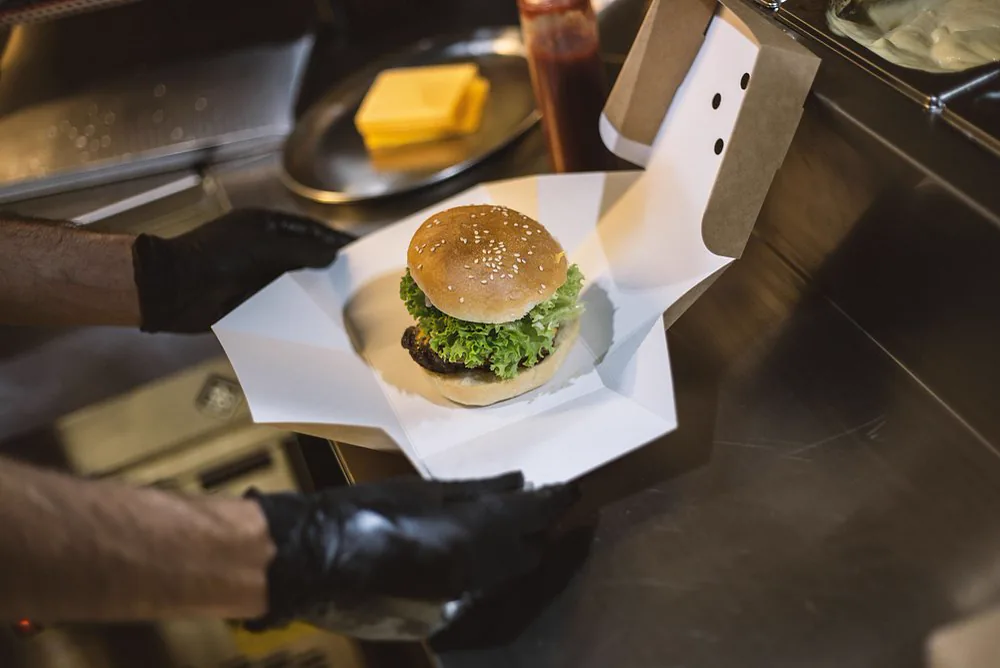 Burger wird mit schwarzen Handschuhen in eine Box gelegt